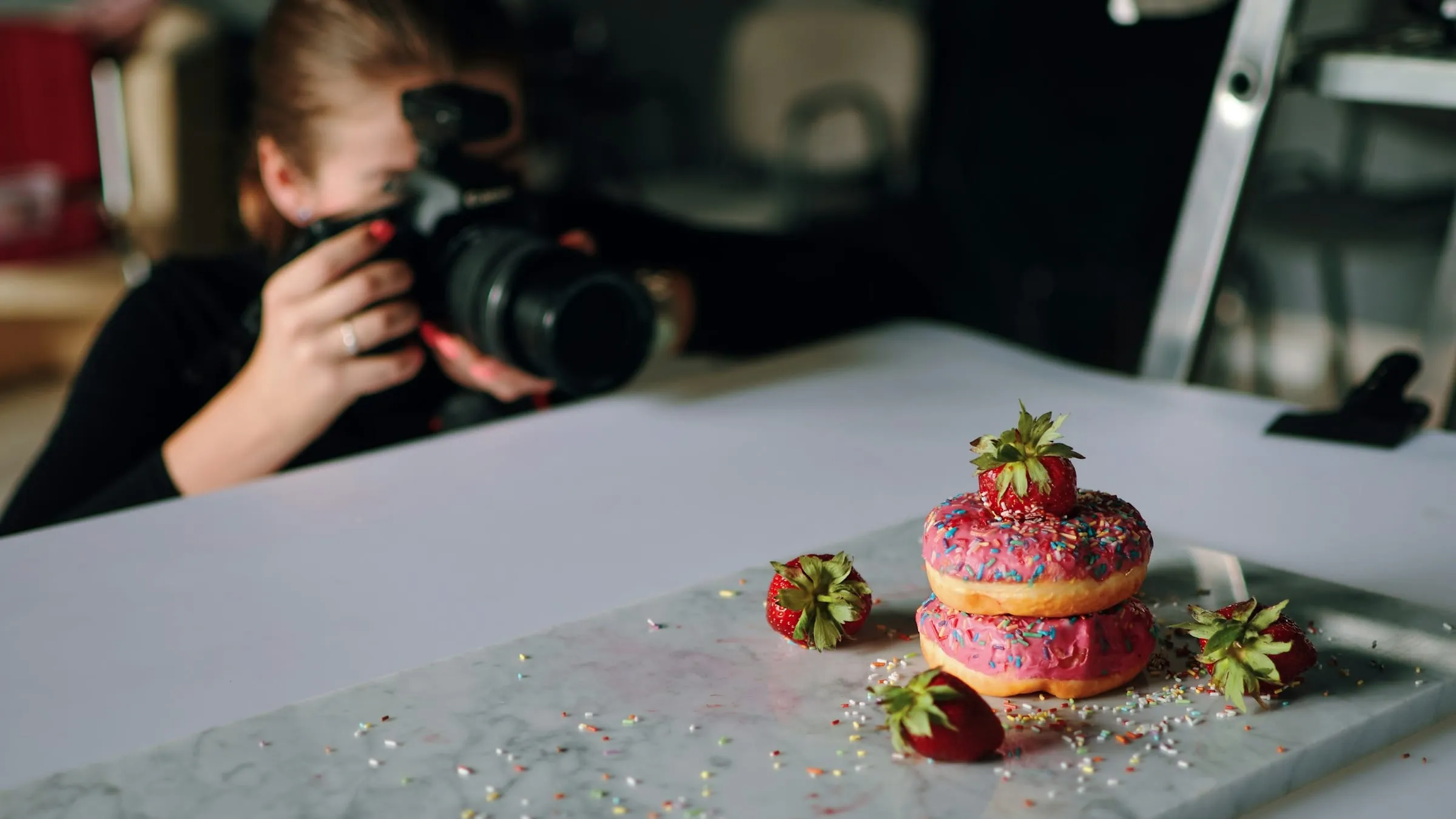 Woman photographing a plate of doughnuts on a marble board for product photos